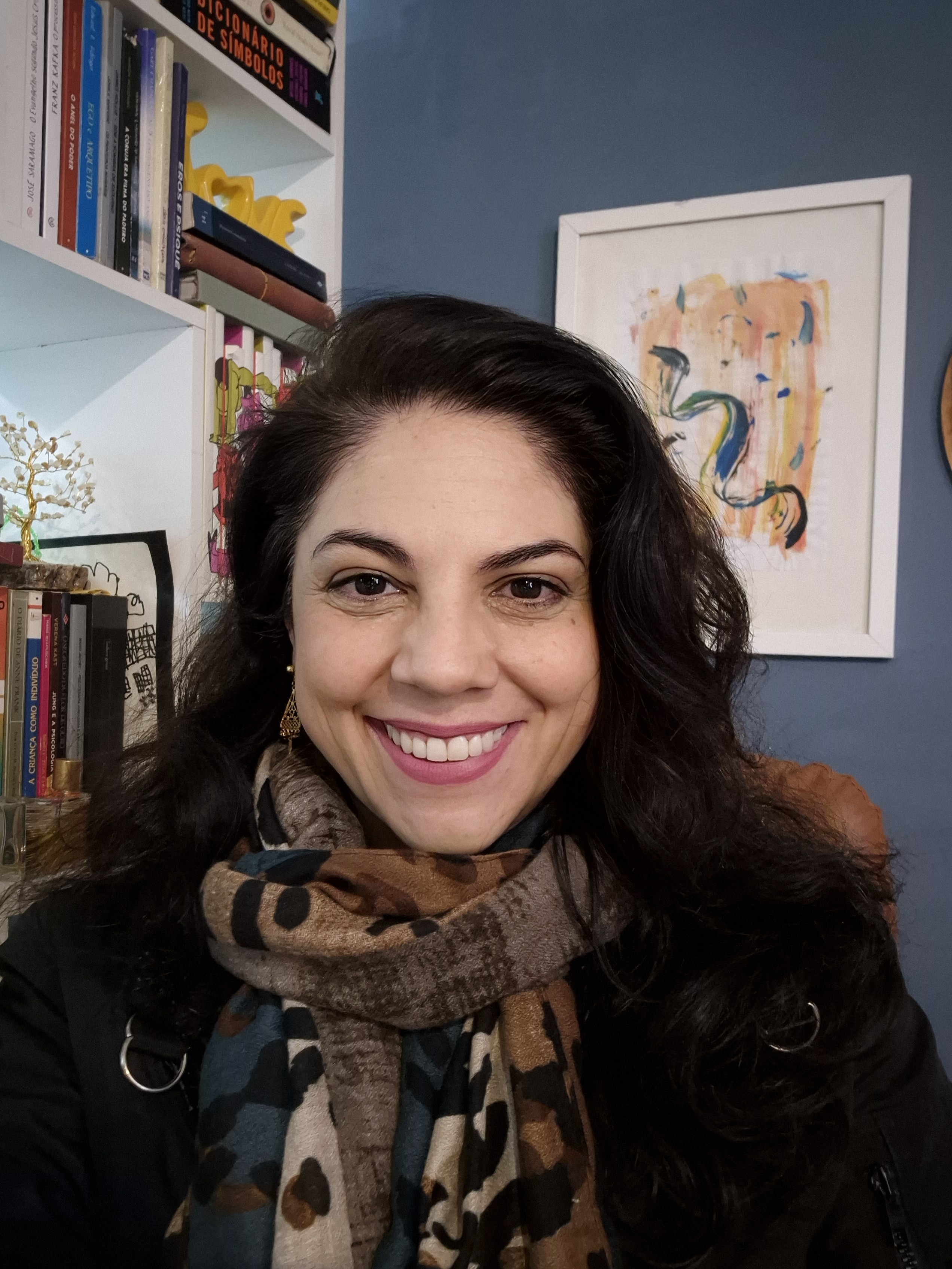 Jac Villa, Jungian psychotherapist, smiling warmly in her office with bookshelves and artwork in the background